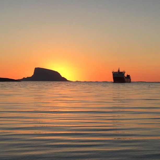 Solnedgang på sjøen med siluetten av en øy som stikker opp og en stor båt på vei ut