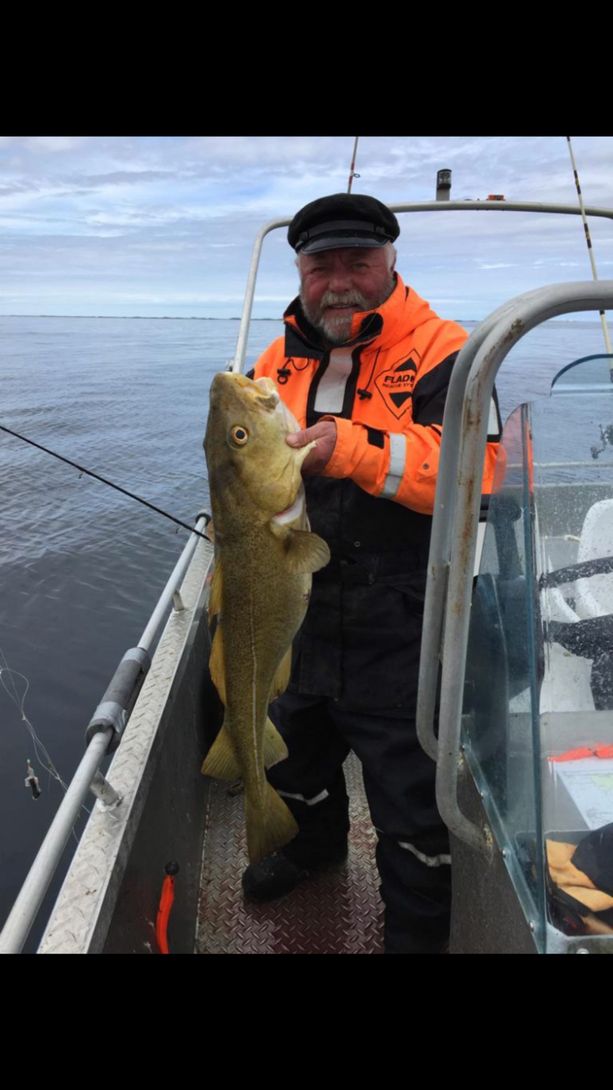 En Bøteriet – Helgeland Rorbuer ansatt som holder opp en fersk fisk etter dagens fangst på en båt på havet